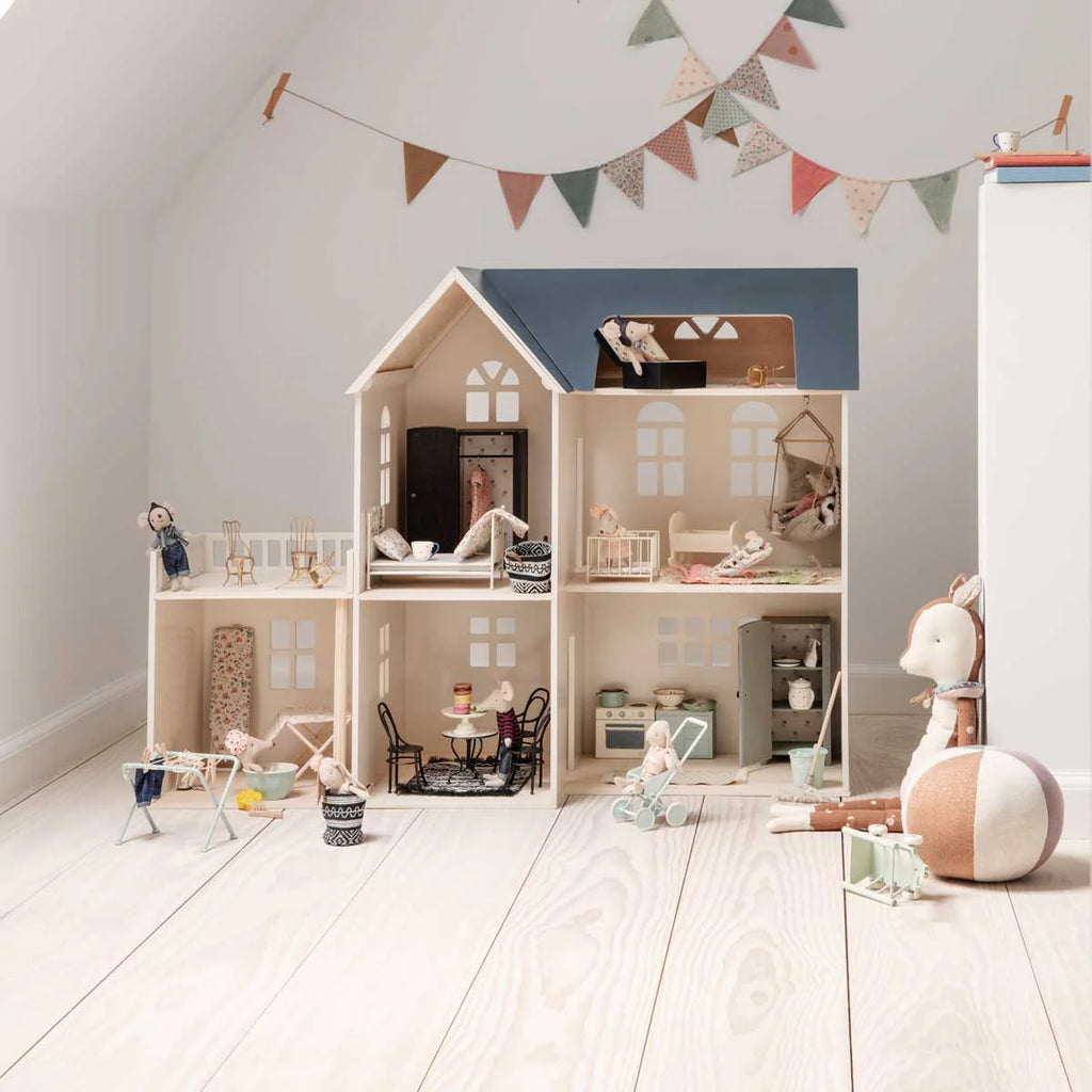 Dollhouse with interior details and toys on a wooden floor, decorated with a string of flags.