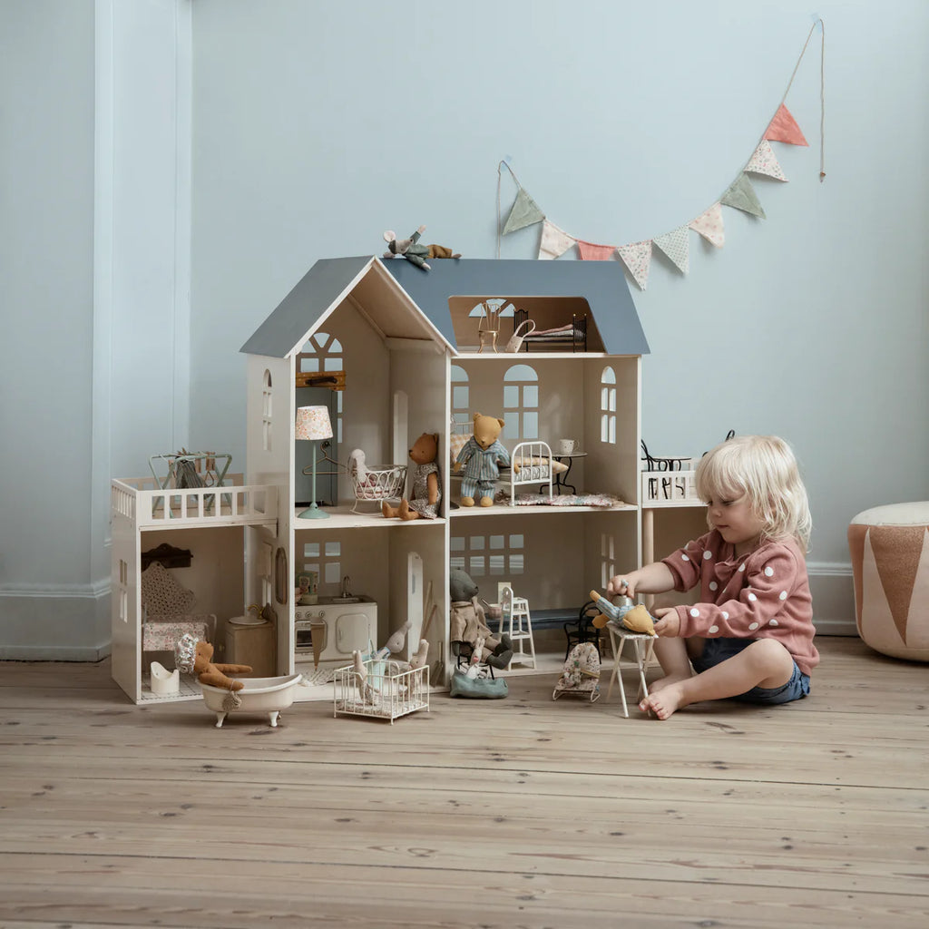 Child playing with a dollhouse in a room with light blue walls and wooden floor.