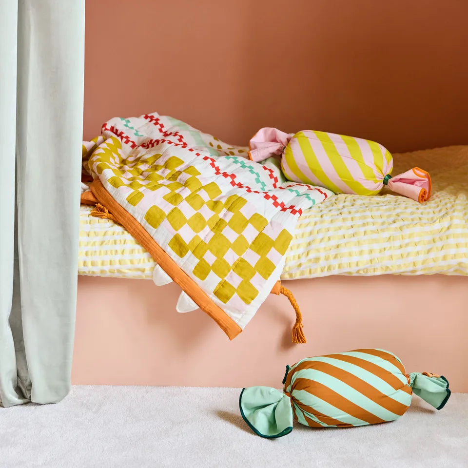 Colorful pillows and cushions on a bed against a pink wall