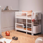Oliver Furniture white Mini+ low bunk bed styled with pink bedding and cushions beside a panelled wall.