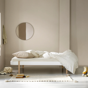 Oliver Furniture Lounger bed in White/Oak styled with pale bedding and a checked duvet beneath a round wall mirror.
