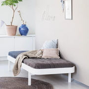 Oliver Furniture white Lounger bed styled with dark checked bedding, pale cushions and a draped blanket against a wall.