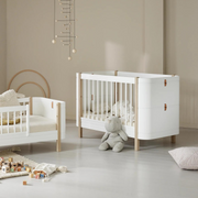 Oliver Furniture Mini+ cot and junior bed configurations in White/Oak styled together with pale bedding and a hanging mobile.