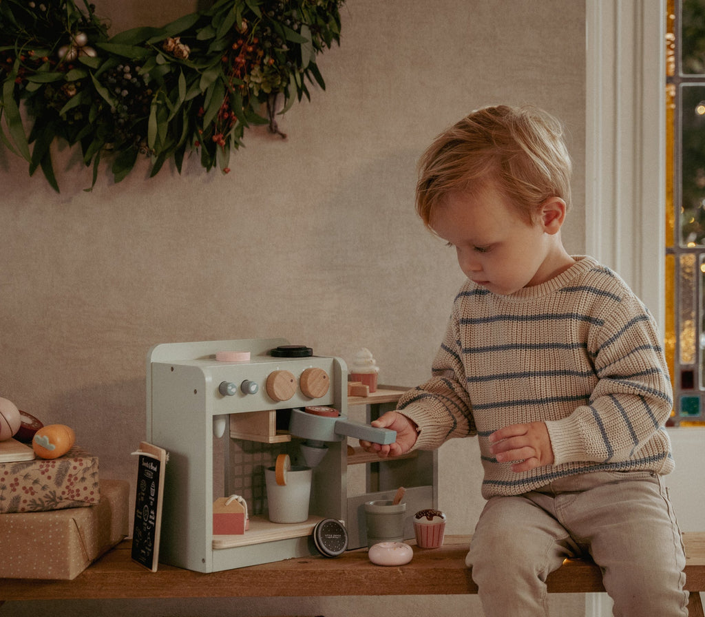 Child playing with a toy kitchen set in a cozy room decorated for Christmas.