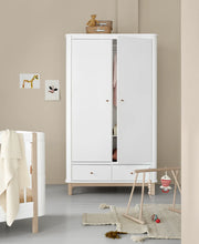Oliver Furniture two-door wardrobe in White/Oak with one door slightly open, styled beside a cot in a pale nursery.