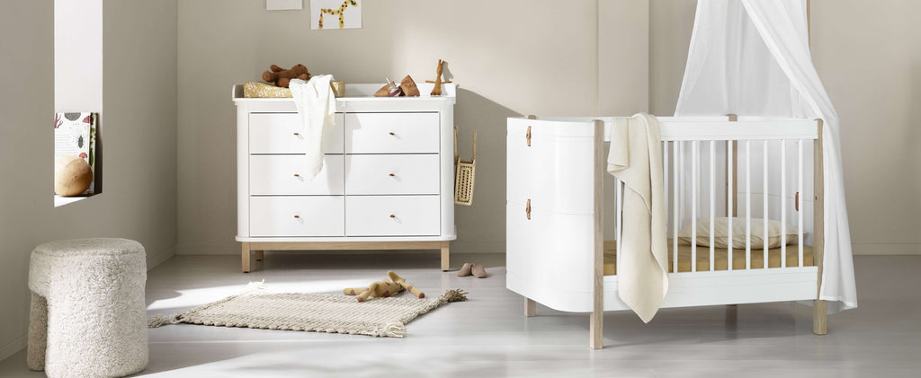 Nursery room with white crib and dresser in a bright room.