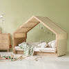A light natural wood house-shaped children's bed with a slanted roof, styled with a striped green and white blanket and patterned pillows in a pale green children's bedroom.