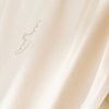 A close-up of draped cream-colored fabric with a subtle, tonal embroidered script logo on the upper left.