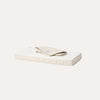 A cream-colored mattress with a folded beige sheet or duvet on top, photographed against a clean white background.