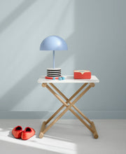 Oliver Furniture Camp bed table in White/Oak with a blue lamp and books on its white top, against a blue wall.