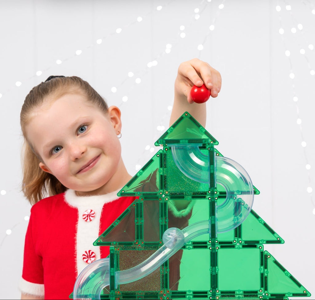 Child playing with a green and clear magnetic building set on a white surface.