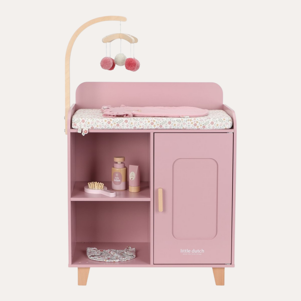 Pink children's changing table with shelves and a cabinet, featuring baby products and a mobile on a white background.
