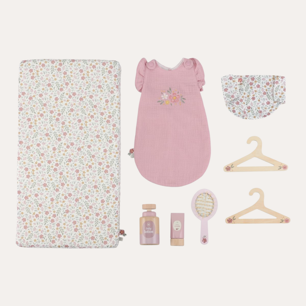 Collection of baby items including a floral blanket, pink dress, and baby care products on a light background