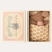 Maileg Rose Sleepy Wakey Baby Mouse tucked under a mustard-patterned blanket in an open illustrated matchbox.
