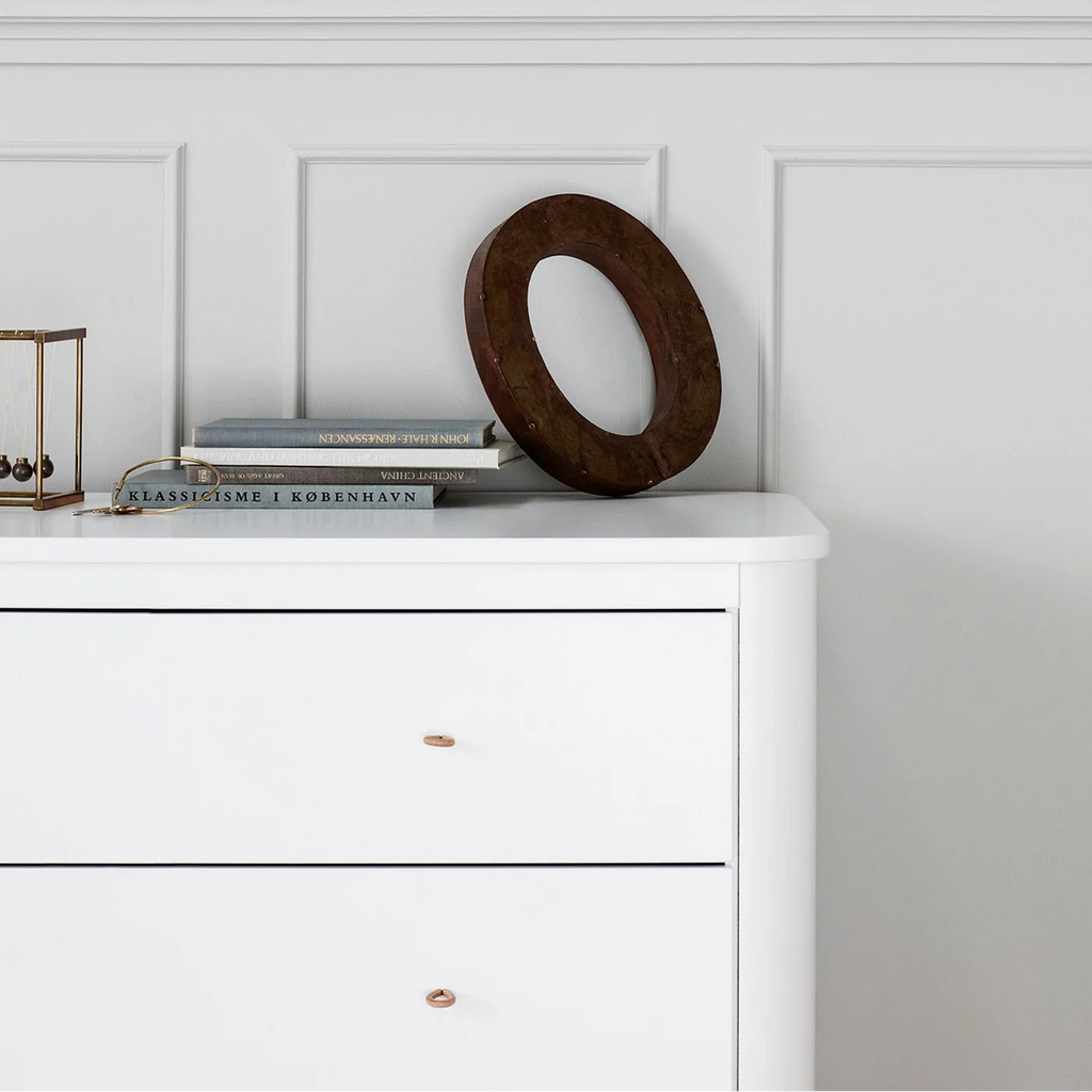 White dresser with decorative items against a paneled wall.