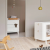 Nursery room with white dresser, crib, and wooden horse toy.