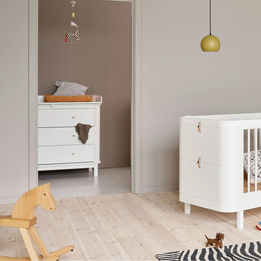 Nursery room with white dresser, crib, and wooden horse toy.