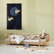 Oliver Furniture Original Floor Bed in Oak with low slatted rails, styled with pale bedding beneath a dark wall hanging.