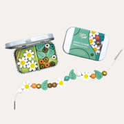 Cotton Twist Daisy Bracelet Gift Kit with an open tin of beads, its lid and a strand of daisy and leaf beads.