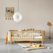 Oliver Furniture Mini+ junior bed in Oak with a front guard, styled with pale bedding and toys beneath a round pendant lamp.