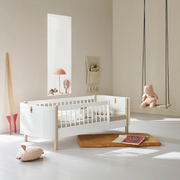 Oliver Furniture Mini+ junior bed in White/Oak with a front guard, styled with bedding near a wall mirror and toy swing.