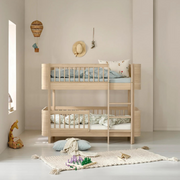 Oliver Furniture Mini+ low bunk bed in Oak with a right-hand ladder, styled with patterned bedding and toys nearby.