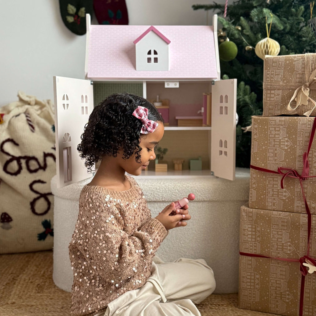 Child playing with a dollhouse next to Christmas presents and decorations.