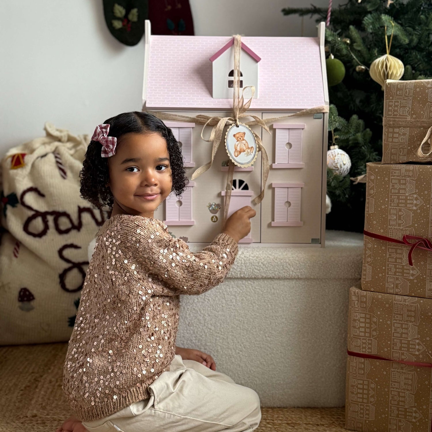 Child playing with a small dollhouse in a festive setting with Christmas decorations.