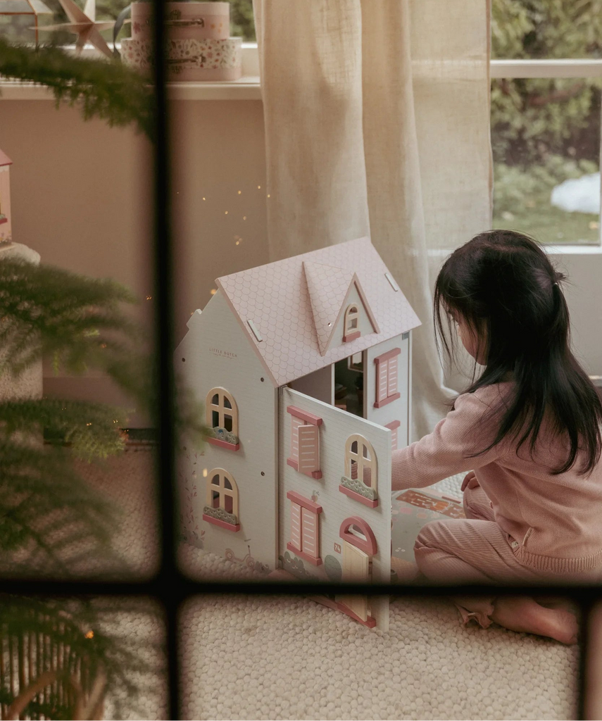 Child playing with a dollhouse in a room with a window and plants.