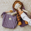 A child tending to a doll on an open lavender Olli Ella Carrie changing bag, with toy care accessories nearby.