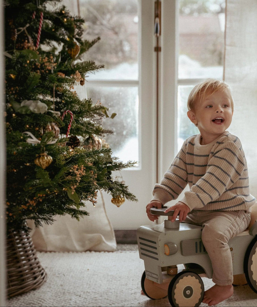 Child playing with a toy truck near a decorated Christmas tree indoors.