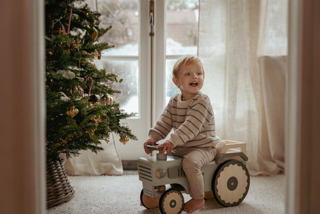 Child playing with a toy truck near a decorated Christmas tree indoors.
