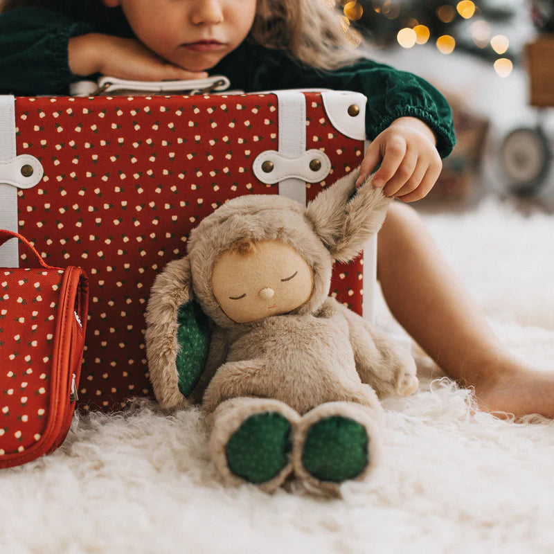 Child holding a red polka dot bag with a plush toy resembling a rabbit on a soft surface.