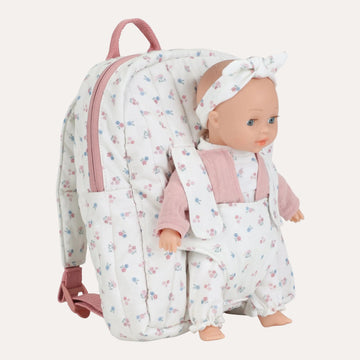 A quilted baby doll backpack with a matching baby doll inside. The backpack is white with a small pink and blue floral print, featuring pink zippers, a pink top handle, and a matching pink bow headband worn by the doll.