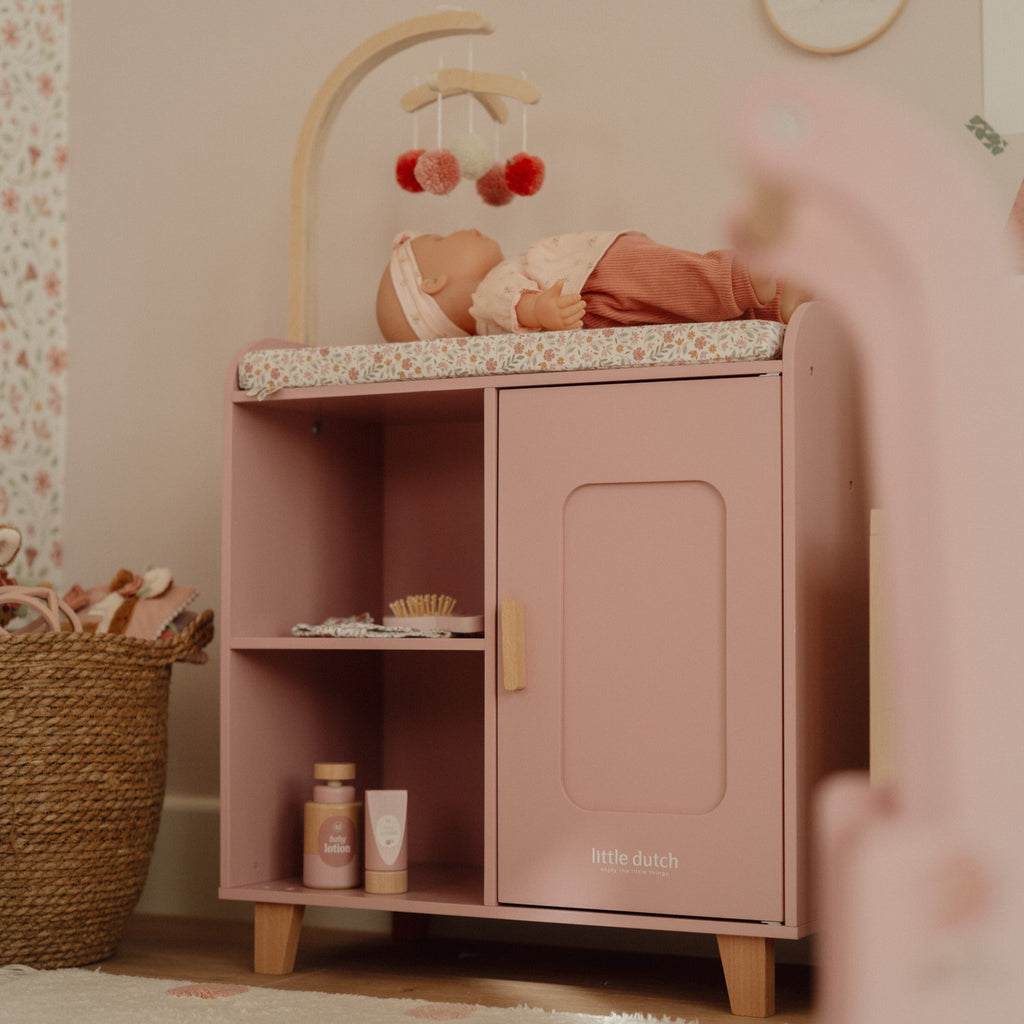 Pink children's cabinet with a baby in a crib inside, in a room with floral wallpaper and decorative elements.