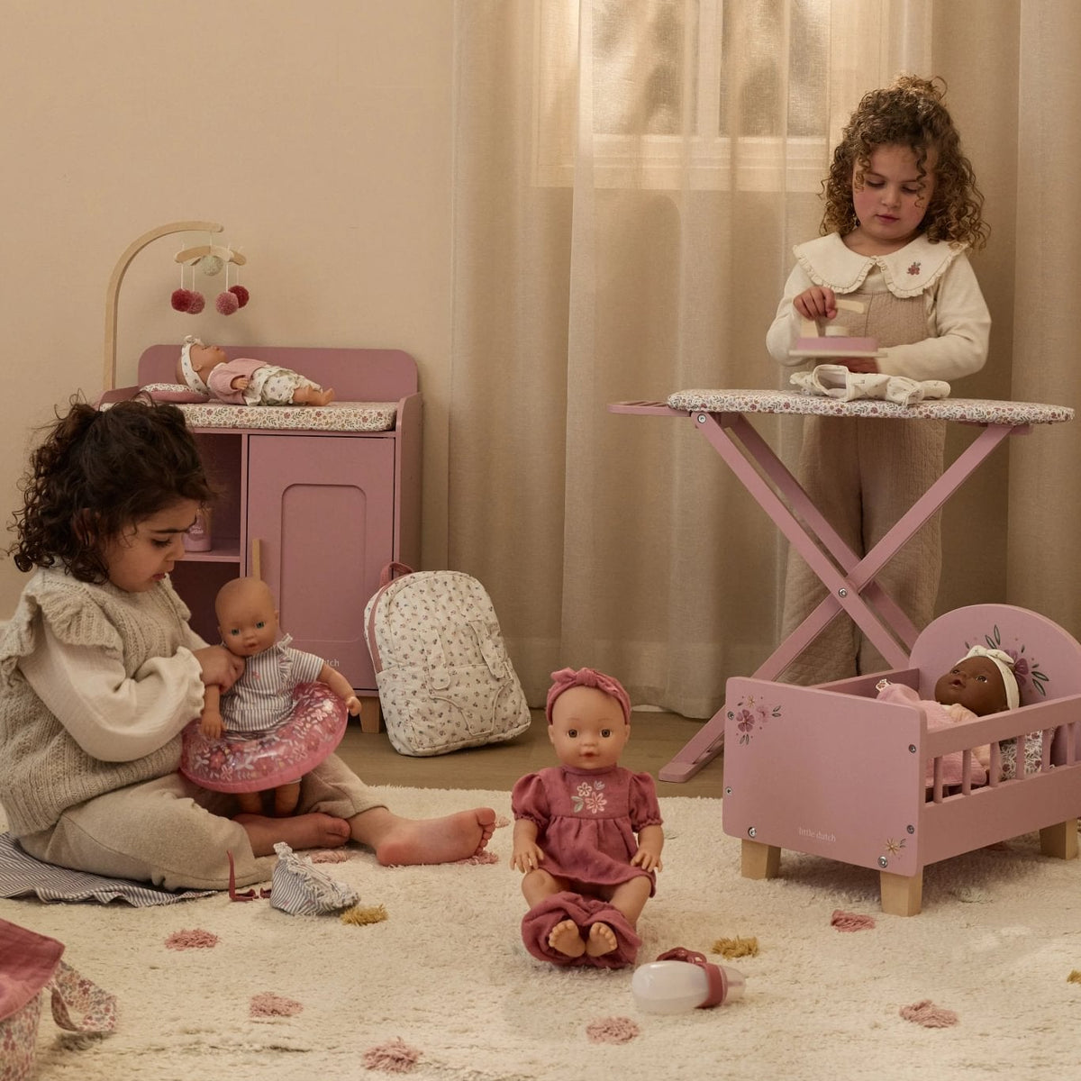 Two young girls playing with dolls in a room with pink furniture and toys.