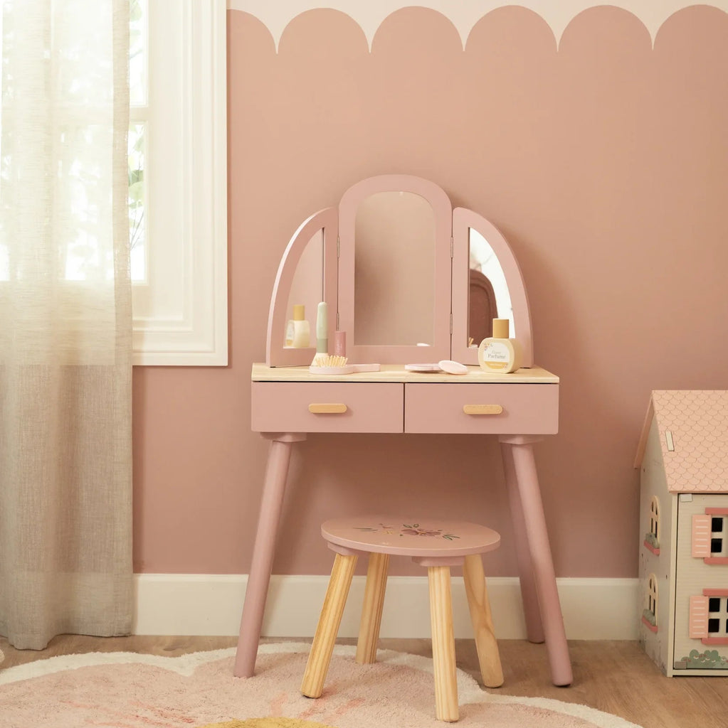 Pink vanity table with mirror and stool against a scalloped pink wall.
