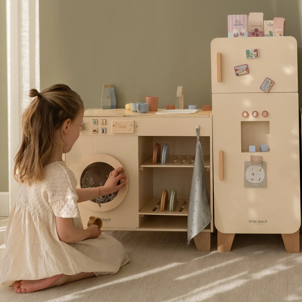 Child playing with a wooden play kitchen set in a room with sunlight streaming in.