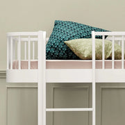 Close-up of the upper bed and ladder on an Oliver Furniture white bunk bed, with blue and green patterned cushions.