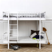 Oliver Furniture white Original bunk bed with a left-hand ladder, styled with pale bedding and dark cushions against a panelled wall.