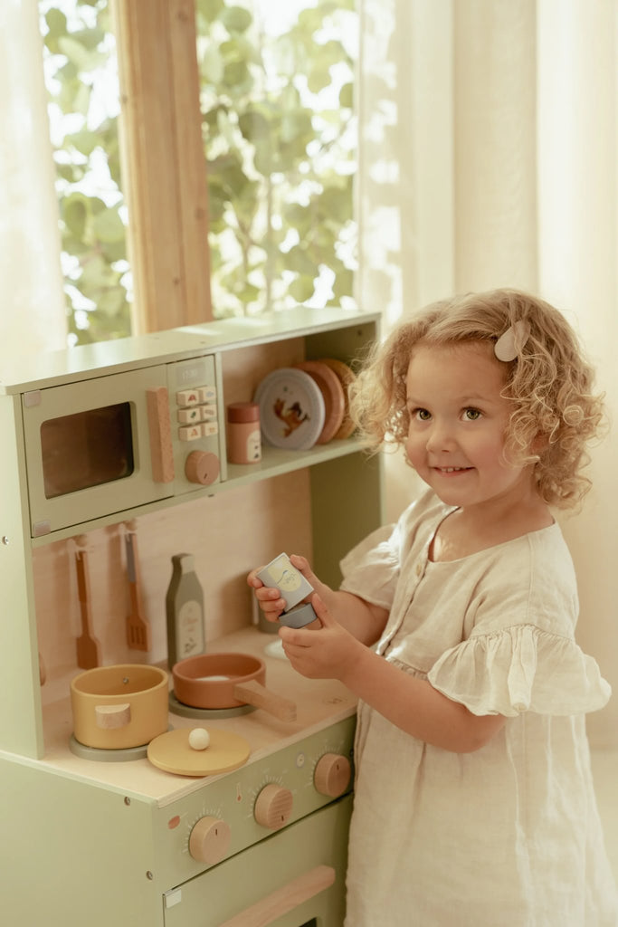Child playing with a wooden toy kitchen set in a bright room.