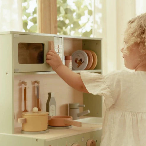 Child playing with a toy kitchen set in a bright room