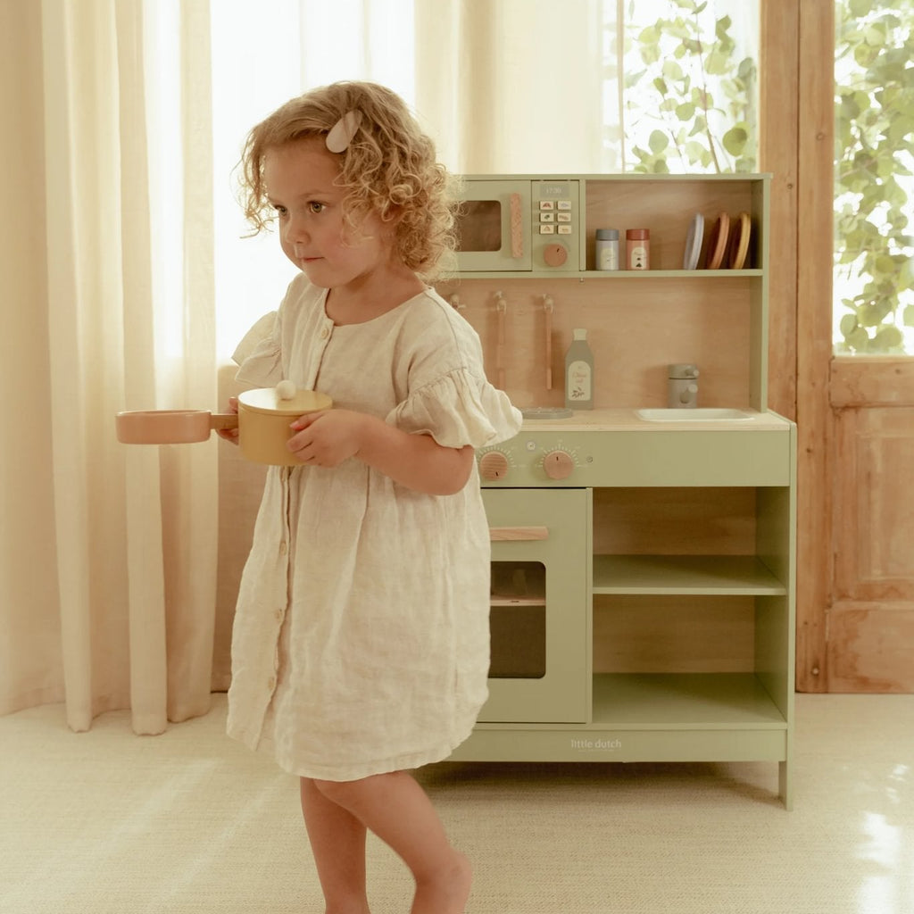 Child playing with a toy kitchen set in a bright room with large windows.