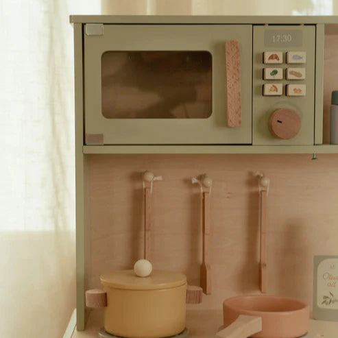 Children's play kitchen set with microwave, pots, and utensils on a light wooden surface.