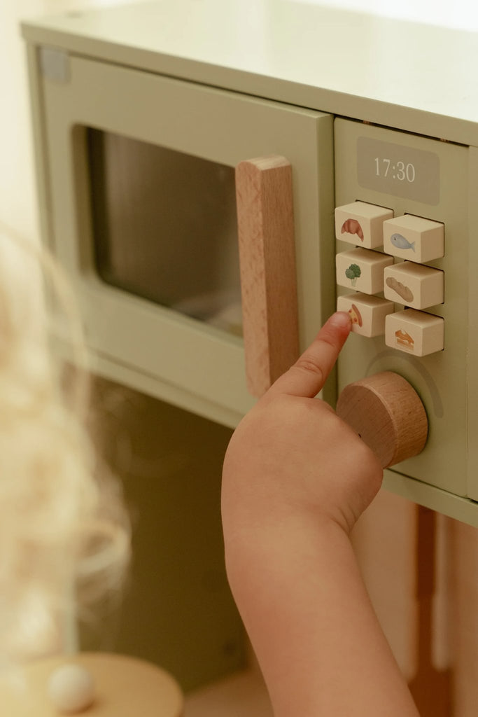 Child's hand pressing a button on a toy microwave oven.