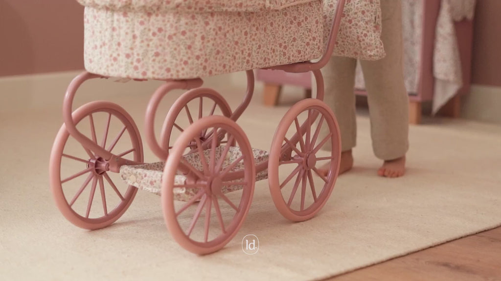 Children playing with a metal doll pram, role playing and pushing her dolly around in a pram
