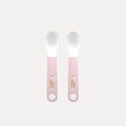Two baby spoons with pink handles featuring deer illustrations on a light pink background.