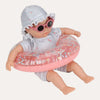 A baby doll wearing a blue and white striped sun hat, matching striped romper, and pink sunglasses, sitting inside a pink inflatable pool float with butterfly patterns on a white background.